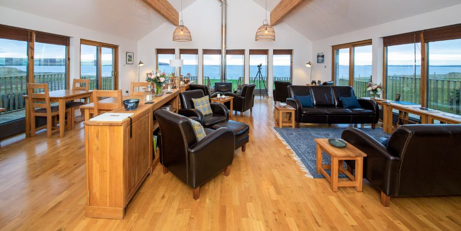 Broadbay House, Isle of Lewis Lounge room with black leather sofas and wood flooring with views out to beach.