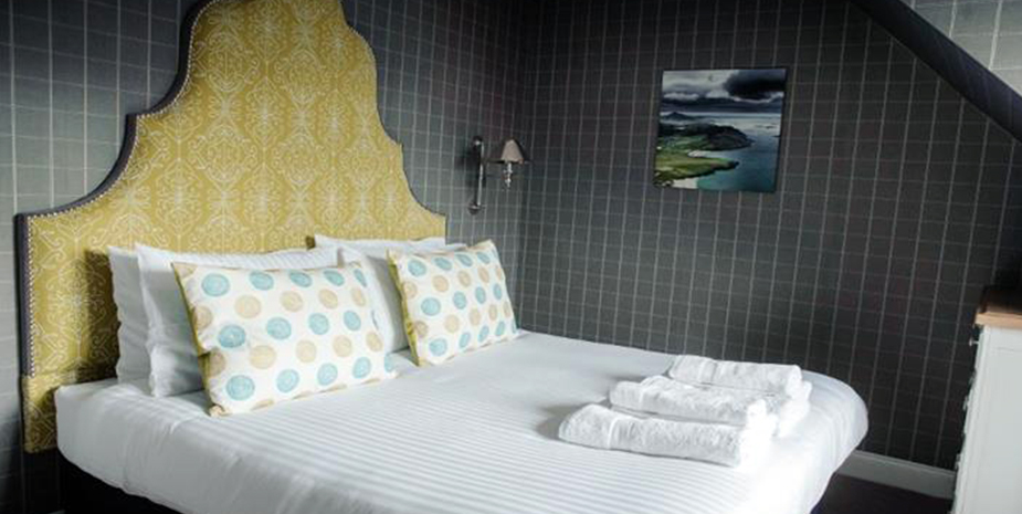 Kirklea Island Suites double bedroom with dark walls, neutral bedding and yellow headboard.