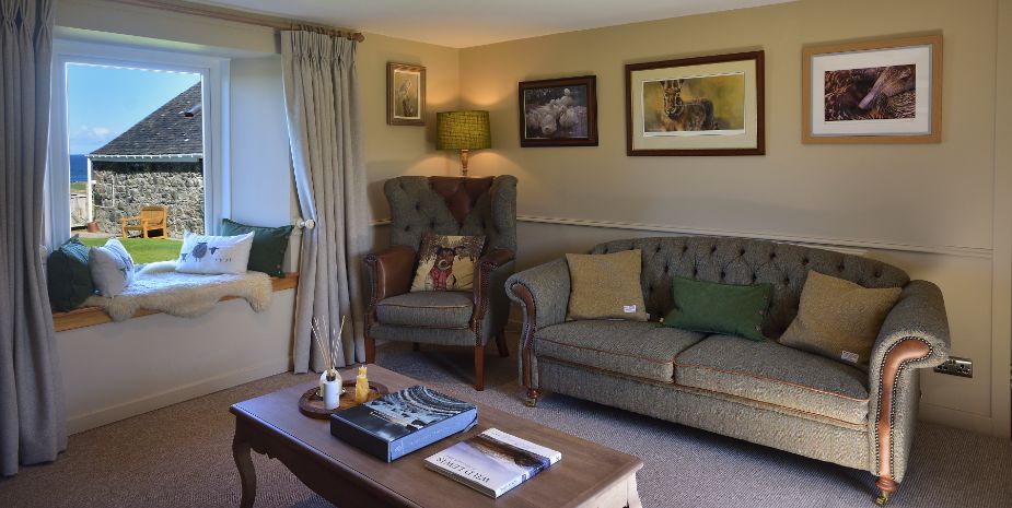 Cosy living room at Galson Farm, Isle of Lewis, featuring a couch, chair, and a bright window.