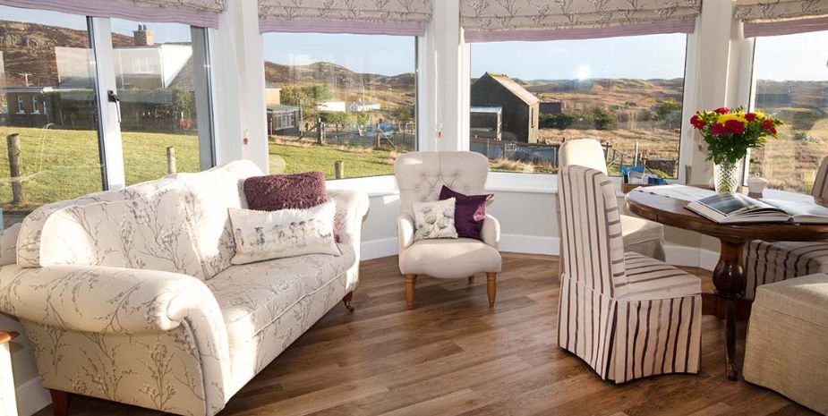 Living room with mountain view, featuring cosy furniture and large windows.