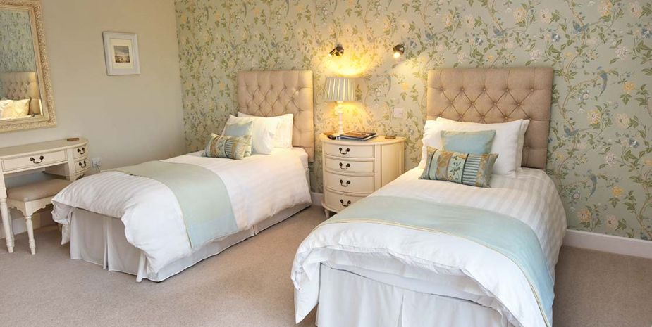 Two beds in a room with floral wallpaper, cosy setting for a relaxing stay.