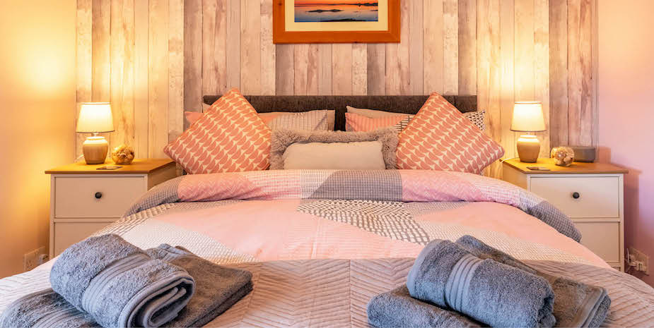 Cosy double bedroom at Ard Buidhe B&B furnished with pink and gray bedding and pillows, set against warm wood-effect walls and Hebridean artwork.