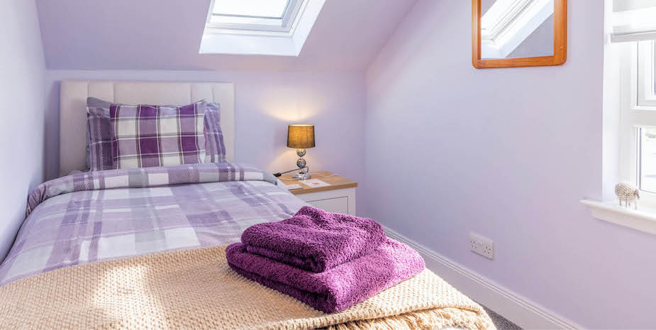 Inviting single bedroom at Ard Buidhe B&B with lilac walls and single bed with lilac furnishings, lit by sunlight streaming through the large windows.