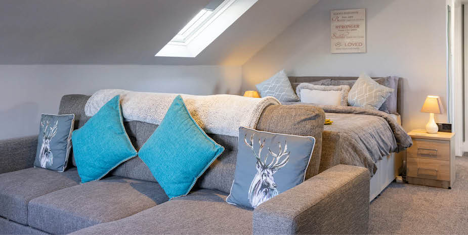 Bright and airy bedroom with a soft grey bed and seating area, perfect for relaxation at Ard Buidhe B&B.