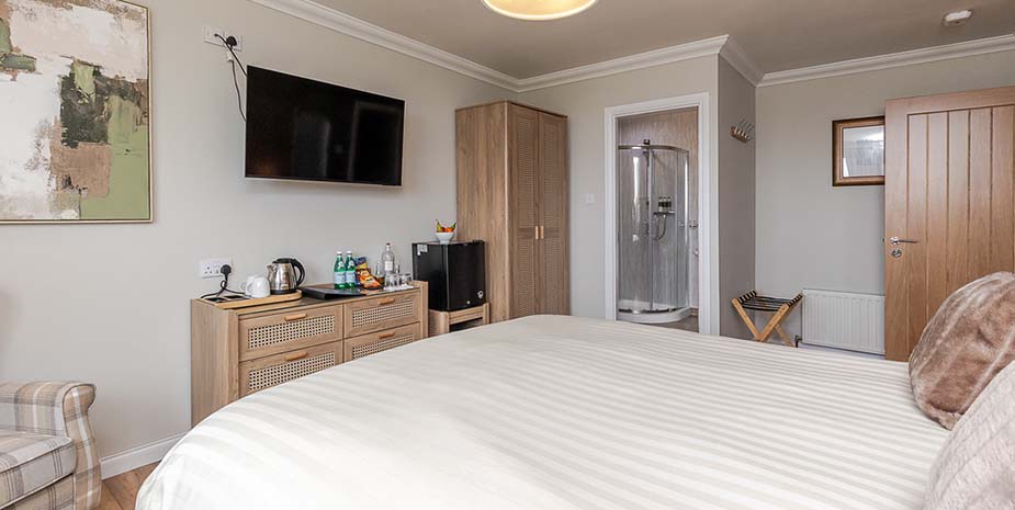 Modern bedroom at Seaview B&B on the Isle of Lewis, featuring a double bed, wall mounted tv, wardrobe, mini fridge and en-suite bathroom.
