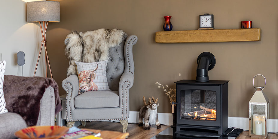 A cosy guest lounge at Seaview B7B on the Isle of Lewis featuring a grey armchair, fur throw, wood burning stove and soft lighting
